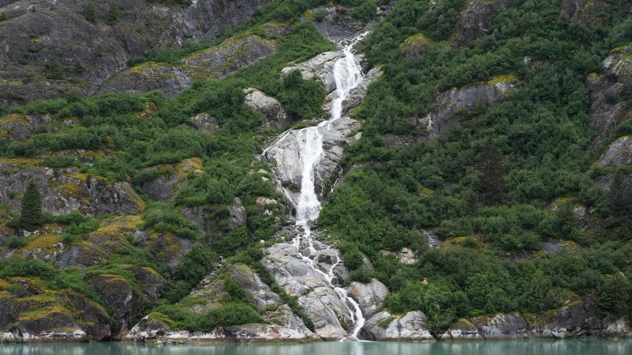 Waterfall's pristine glacial meltwater plunges into the emerald waters of Endicott Arm fjord, Alaska.