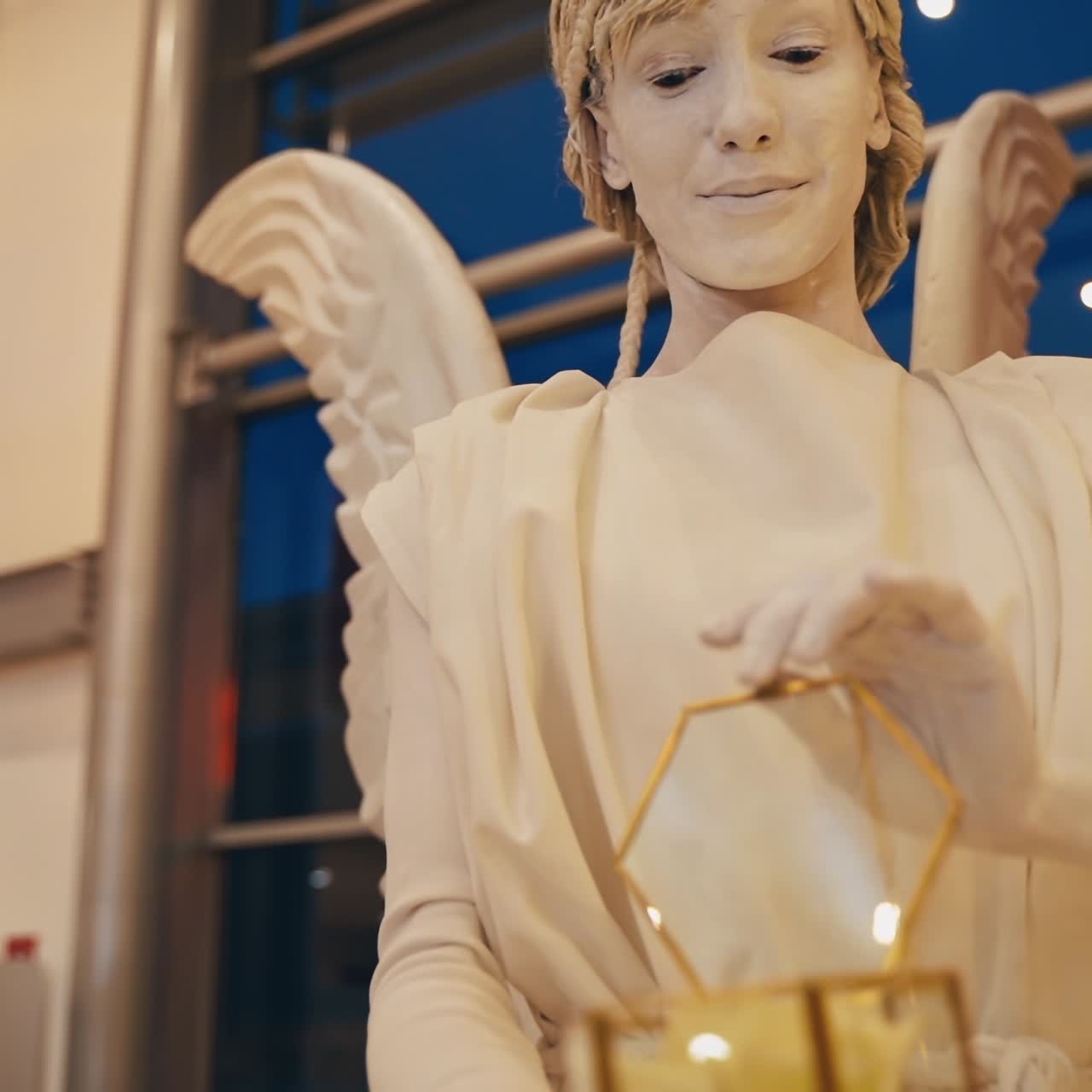 Alive sculpture outdoors. Beautiful living statue angel opens glass box with nice flower inside. Live white statue.