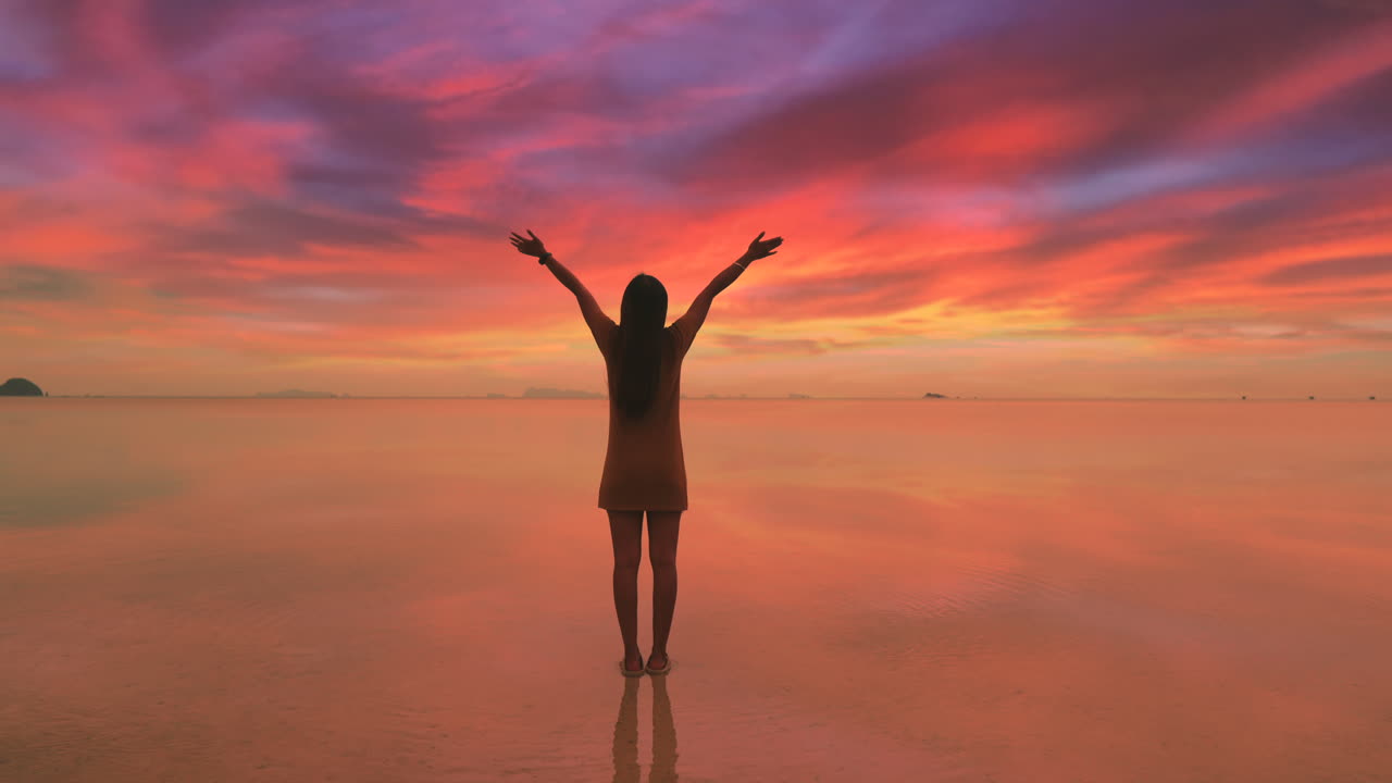 chica feliz levantó las manos arriba permanece en la superficie del agua tranquila mirando la increíble puesta de sol del mar celebrar el momento de la vida