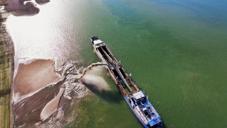 Toma-Aérea-Superior-De-Una-Draga-Descargando-Arena-Dragada-En-Un-Gran-Río,-Día-Soleado