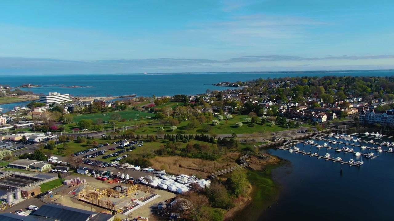 Ripresa con drone che sale e scende verso destra sopra un quartiere sul lungomare, un porto turistico e un paesaggio costiero durante una giornata primaverile a Stamford, Connecticut
