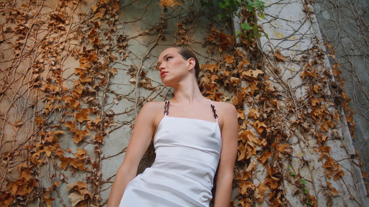 mujer inclinada en un viejo edificio cubierto de follaje de otoño.