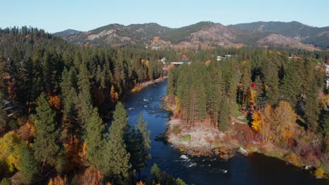 Aerial-view-of-small-rural-town-on-the-banks-of-fast-blue-river-surrounded-by-forest-in-Washington,-USA