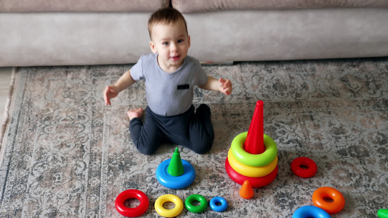 Active Caucasian toddler jumps on the floor. Toy pyramids on the floor in front of baby. High angle view.