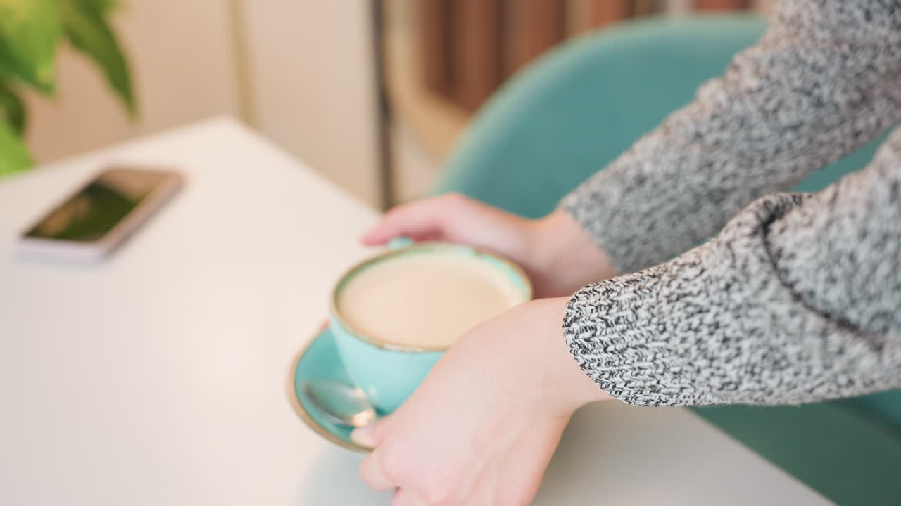 close up of young female freelancer approaching table breakfast in hands bending gently placing cup and saucer adjusting mock tray and mock with care sitting down relaxed in cozy indoor setting