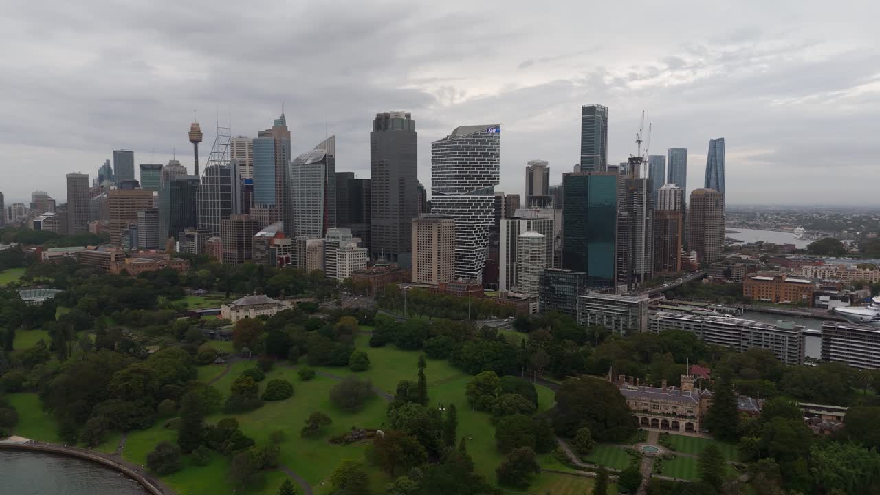 Aerial left orbit reveals Sydney’s modern CBD skyline rising behind the lush greenery of the Royal Botanic Garden, blending urban architecture with waterfront parkland in New South Wales, Australia.