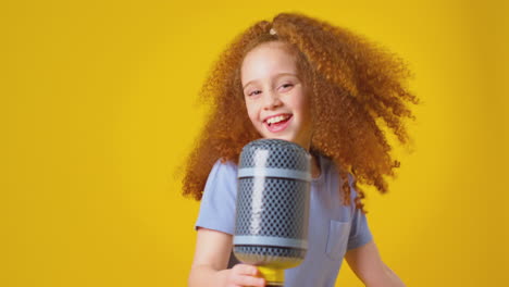 studio shot of girl singing karaoke into inflatable microphone against yellow background