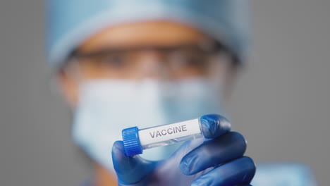 close up of female lab research worker wearing ppe holding test tube labelled vaccine