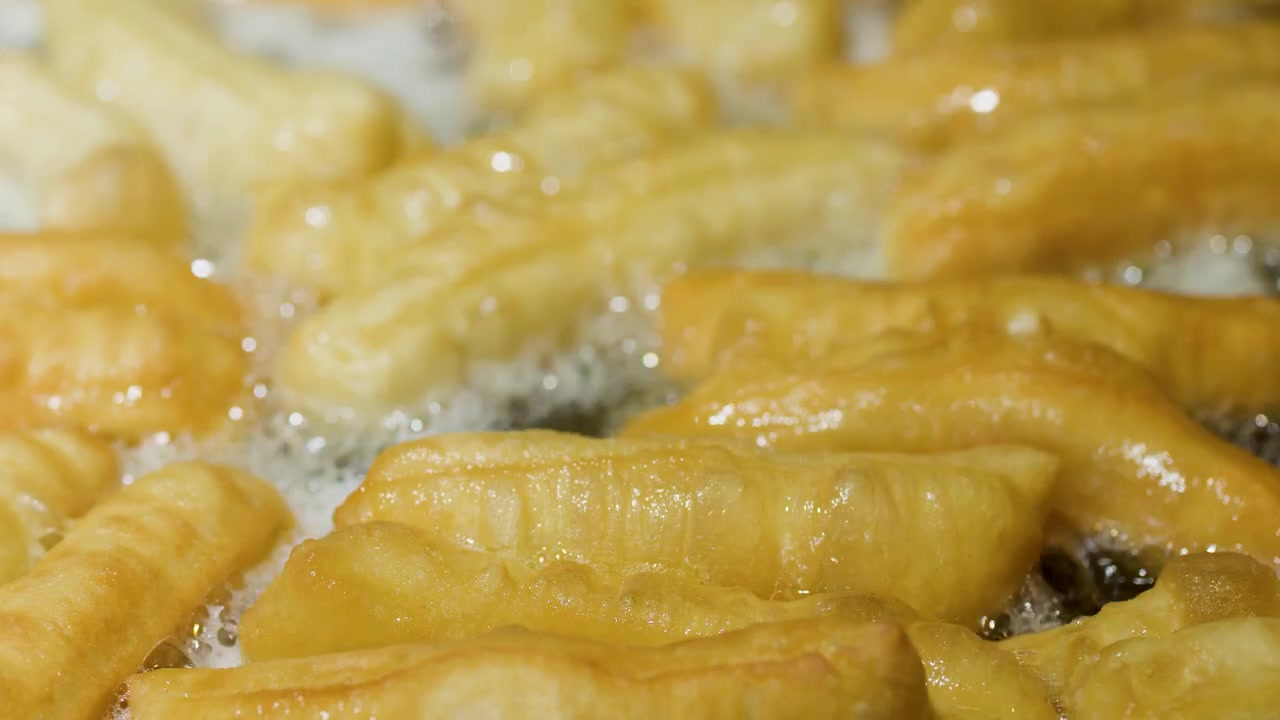 Primo piano di bastoncini di pasta youtiao dorati che friggono in olio bollente durante la preparazione di cibo da strada