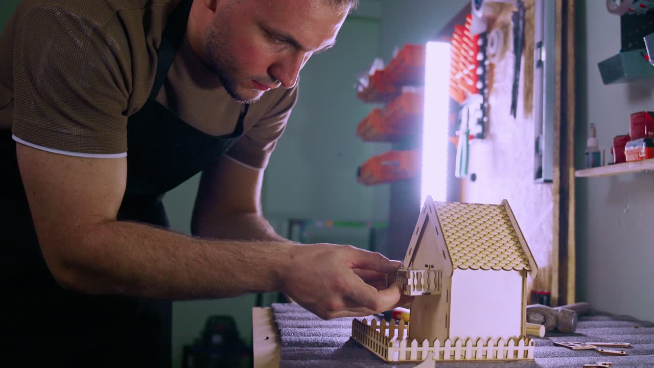 Man Assembling a Detailed Wooden Model House in a Workshop