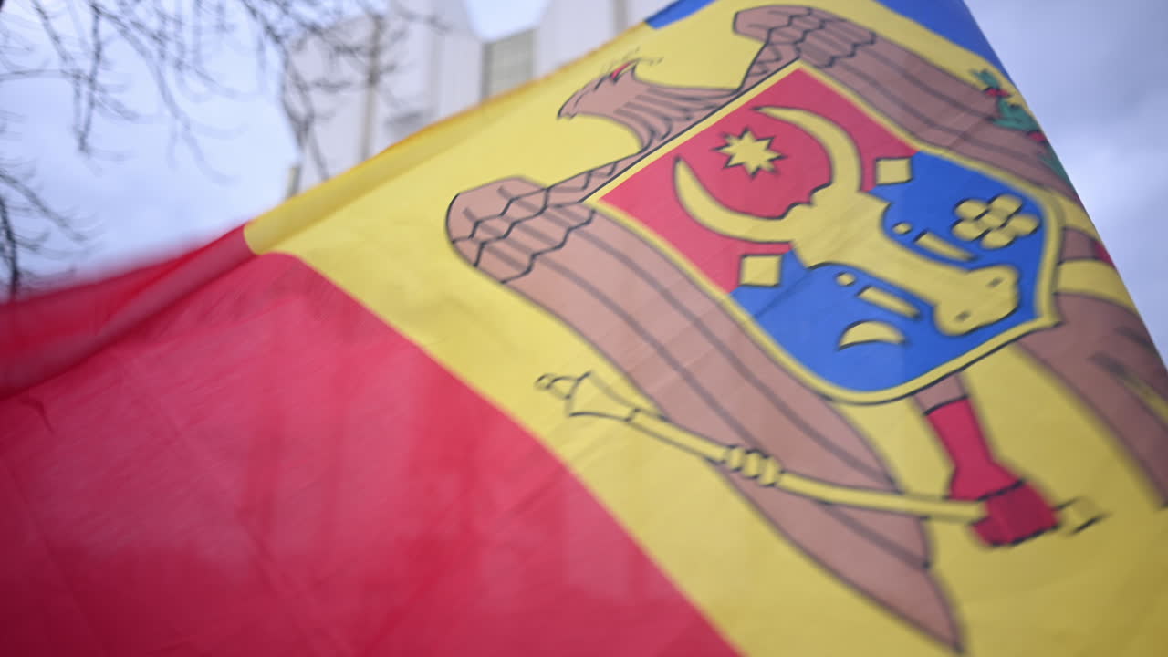 Close-up da bandeira nacional da Moldávia tremulando ao vento com o brasão de armas visível.