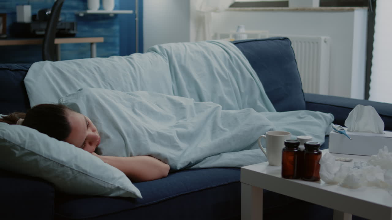Sick woman laying on couch with blanket feeling cold