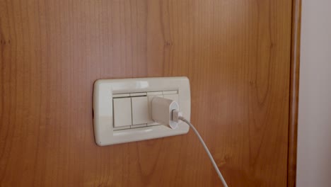 close-up of a hand inserting a power plug into a wall socket. concept of electricity, energy use, connection, charging electronic devices and daily household activity