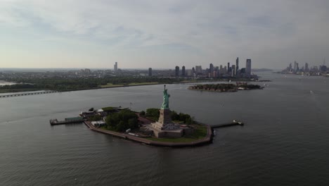 Vista-Aérea-Alrededor-De-La-Estatua-De-La-Libertad-Con-El-Fondo-Del-Horizonte-De-Nueva-Jersey-Y-Manhattan-En-Nyc,-Usa---órbita,-Disparo-De-Drones