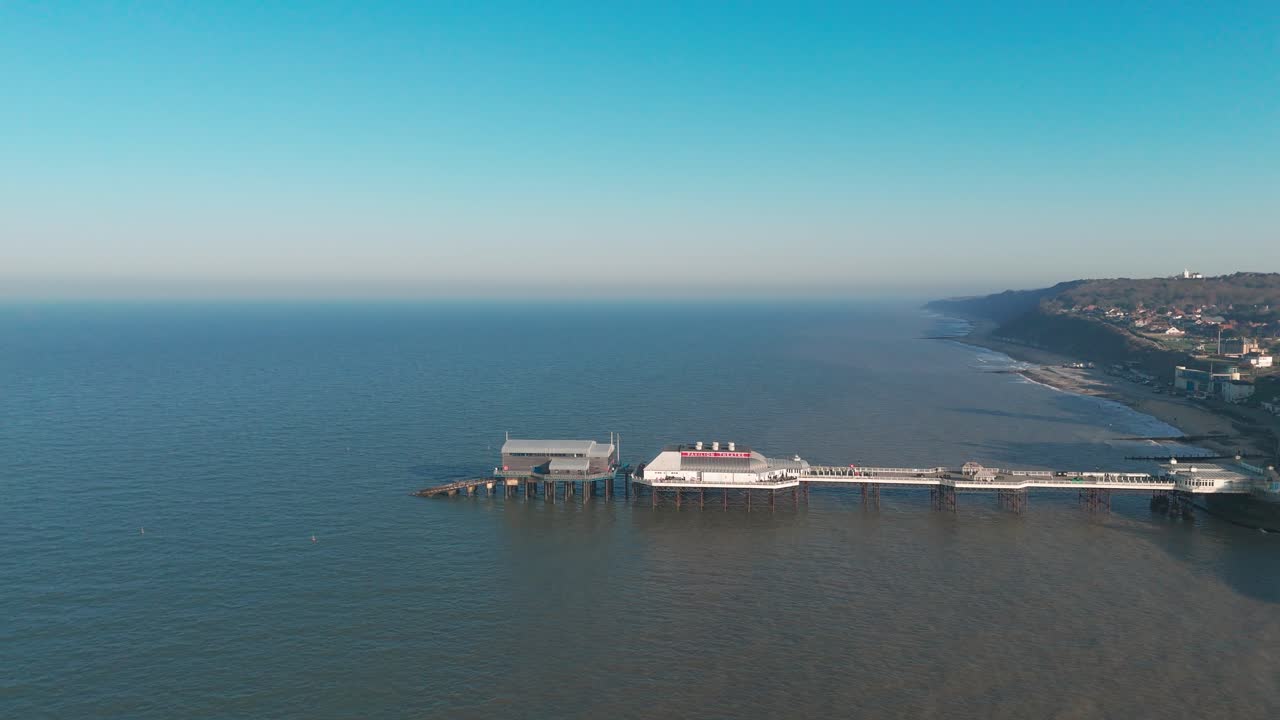 Cromer Pier extending into the calm sea, with a coastal town and cliffs in view