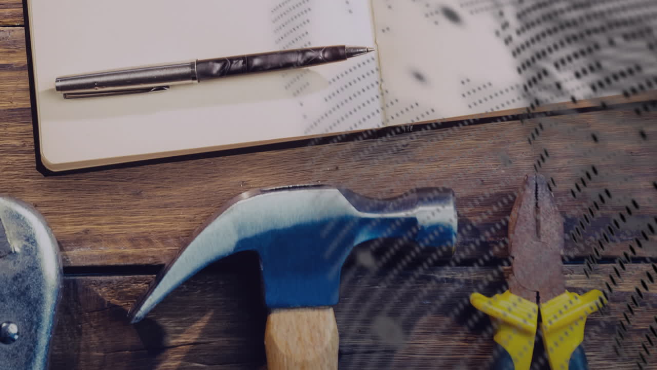 On wooden table, hammer and pliers beside notebook and pen for animation