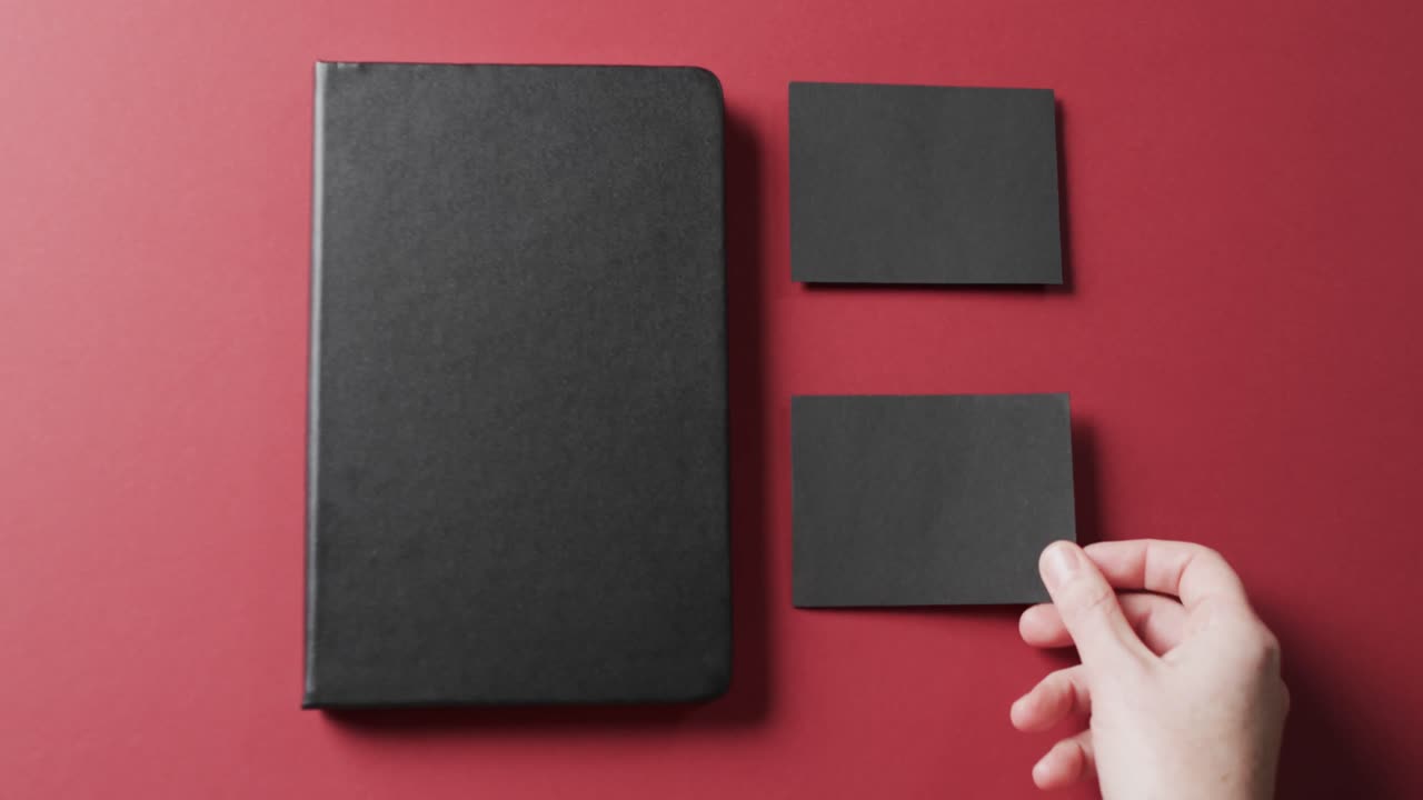 Video of caucasian woman putting black paper cards with copy space and notebook on red background