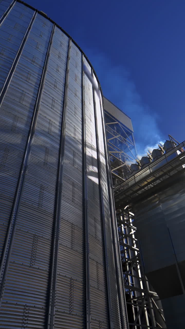 Large granary outdoors. Modern industry with aluminium grain elevators in a bright summer day. Silver silo shining in the sun. Close-up. Vertical video