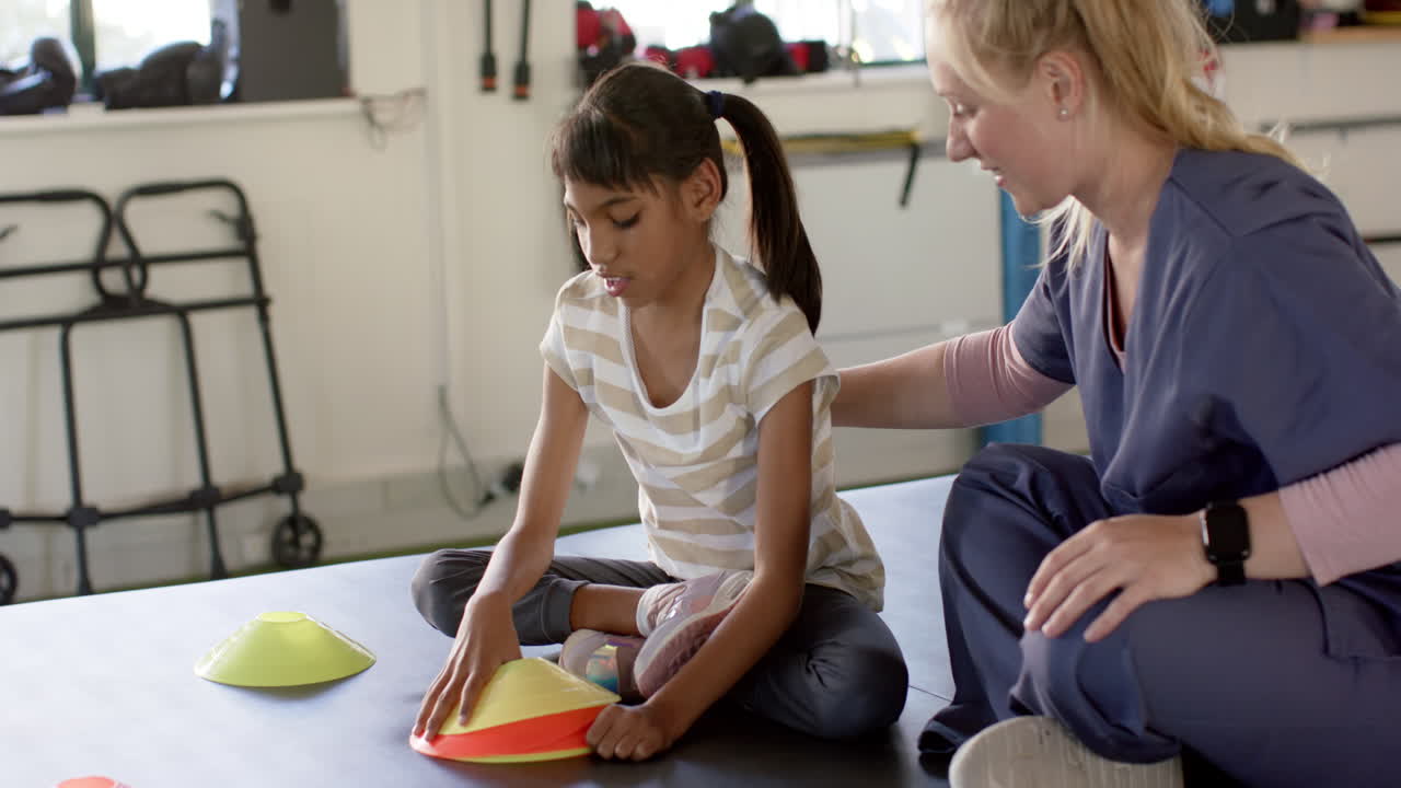girl with cerebral palsy in disability rehab, playing with therapy cones, assisted by therapist