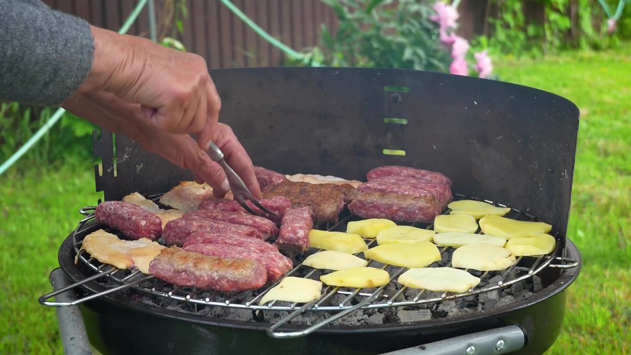 Persona che griglia mici tradizionali rumeni con patate su un barbecue a carbone in un giardino di casa durante l'estate