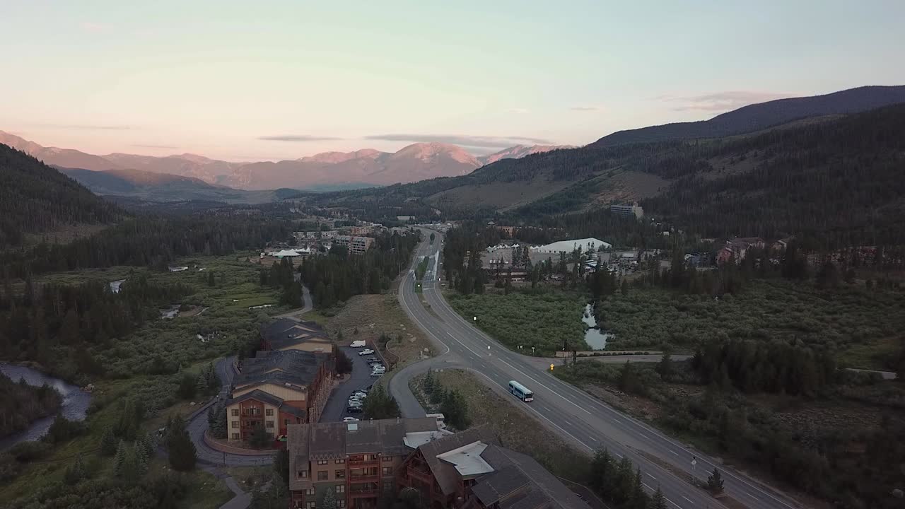 aerial shot - descending on a lone road through the rocky mountains at sunset