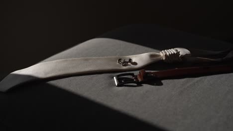 Groom's-white-suspenders-and-brown-leather-belt-laid-out-on-a-bed-in-sunlight