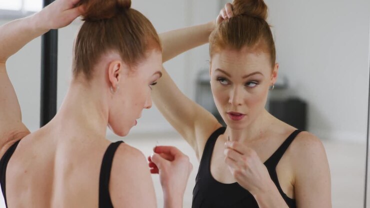 Caucasian female ballet dancer preparing for dance class in a bright studio