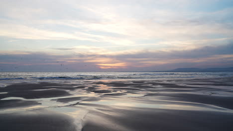 soft sunlight illuminates a serene beach scene as gentle waves wash over the shore, creating reflective pools on the wet sand under a pastel sky