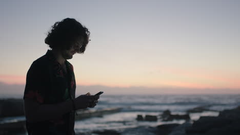 young man using phone texting by seaside waiting sunset sunrise