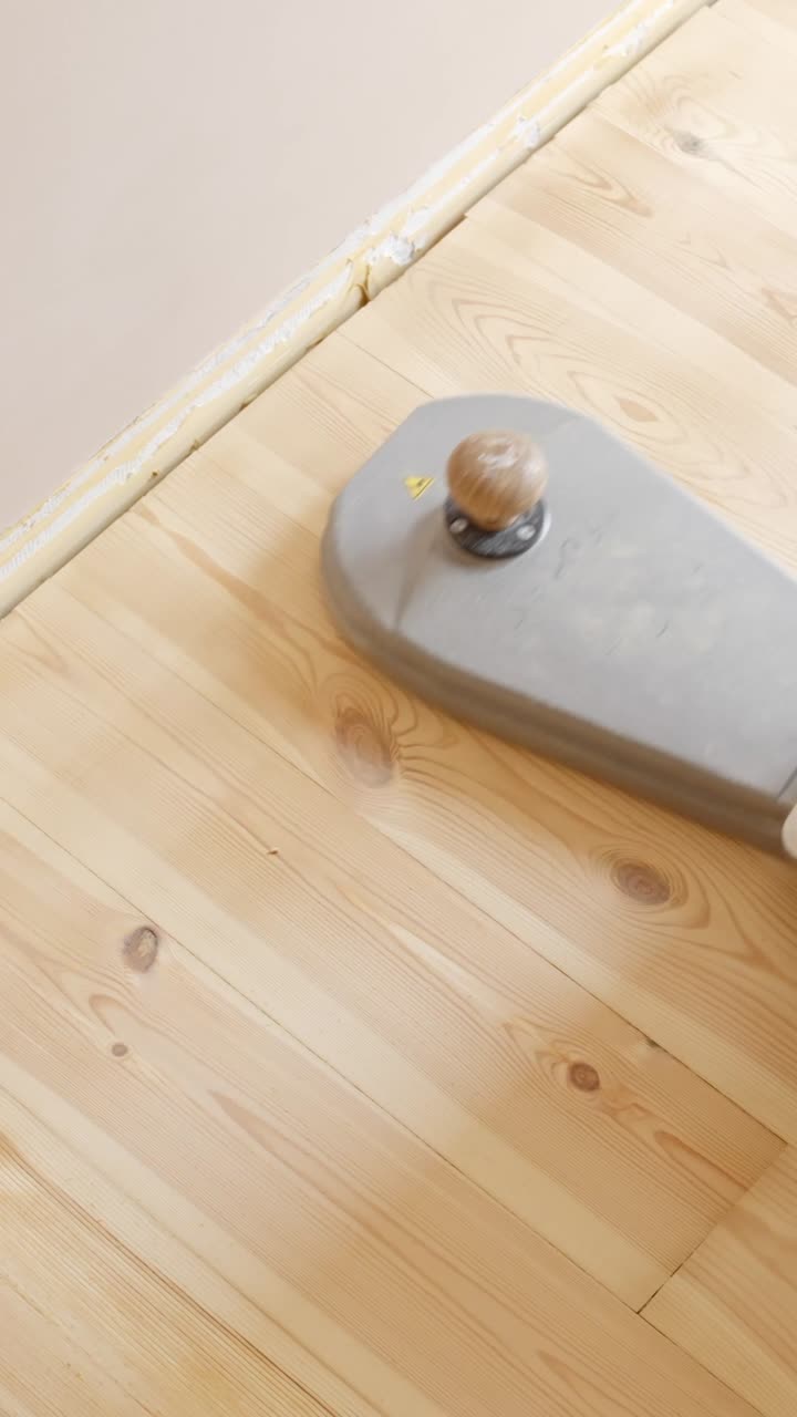 Sanding the edges of a wooden floor using a handheld machine in an interior space