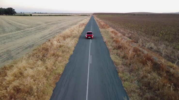 Il drone sale lentamente mentre un'auto rosso vivo percorre una strada di campagna pianeggiante