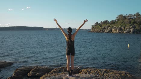 Toma-Amplia-De-Mujer-Joven-Haciendo-Yoga-En-Ropa-Activa-Junto-Al-Agua