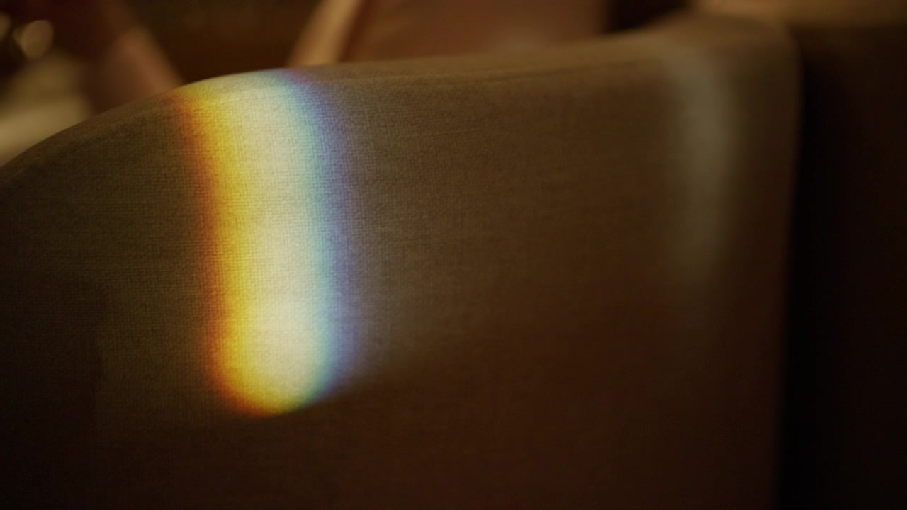Close-up de um reflexo prismático semelhante a um arco-íris caindo sobre uma cadeira de restaurante de tecido bege.