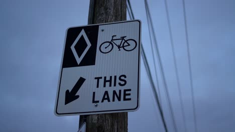 hov bike lane diamond sign on wooden post in urban area with exposed telephone wires and electricity lines - sign for bikers, cyclists, and bicyclists - road rules and signs for bicycles on cloudy day