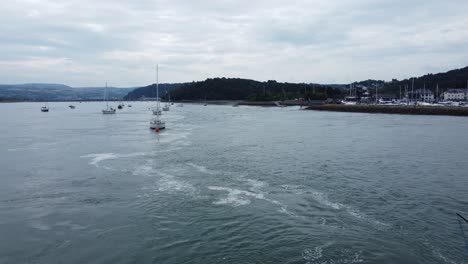 Scenic-Welsh-coastal-village-resort-with-river-boats-anchored-across-the-waterfront-aerial-flyover