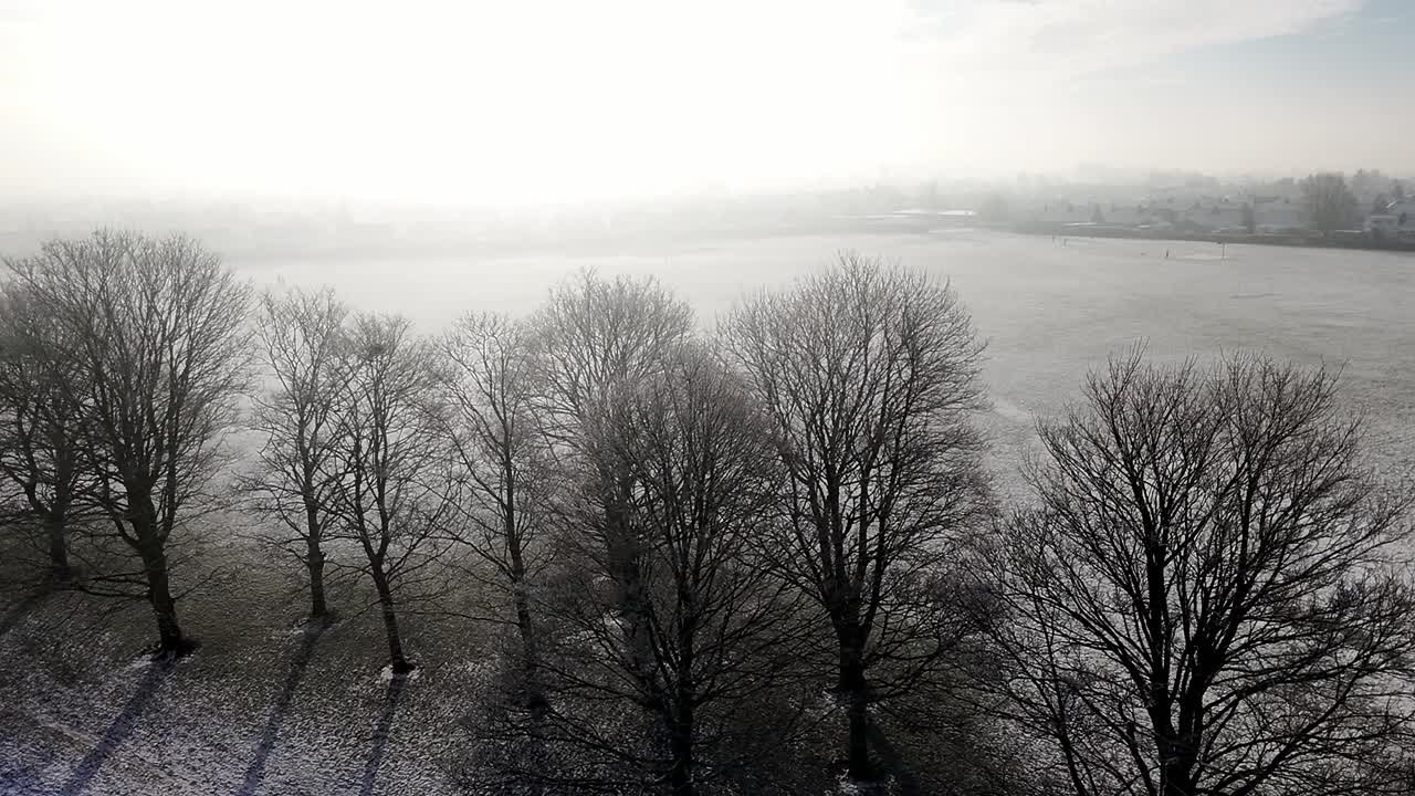 Aerial view descending across misty frozen English winter public park illuminated by morning sunrise