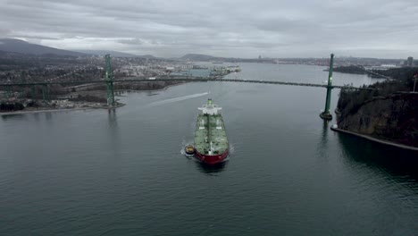 Barge-and-pilot-boat-passing-under-First-Narrows-or-Lions-Gate-Bridge-with-landscape-in-background