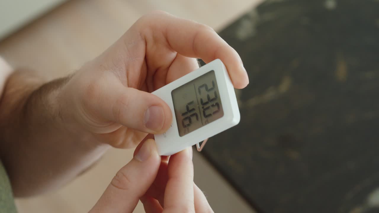 Close-up of a hand holding a digital thermometer and hygrometer, checking indoor temperature and humidity levels to prevent mold growth and maintain a healthy home environment