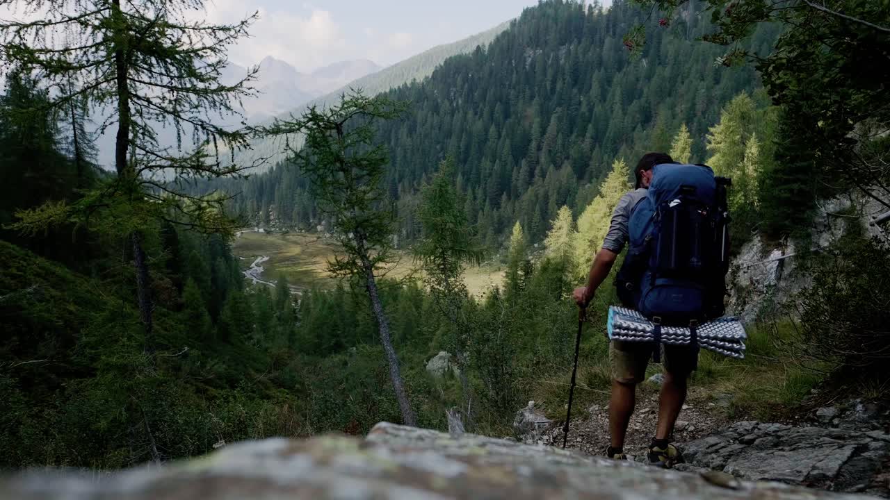 Static medium shot of active Man Hiking Downhill With Trekking Poles in the Dolomites of Italy in summer