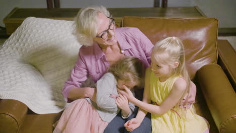 top view of grandmother hugging to her two granddaughters sitting on the sofa while talking in the living room at home 1