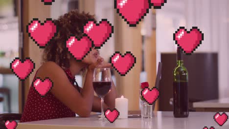 animation of heart icons over happy biracial woman with wine having laptop video call