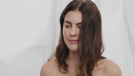 slow motion portrait of attractive caucasian woman smiling running hand through hair wind blowing beautiful female with silky soft skin complexion enjoying natural beauty in white background