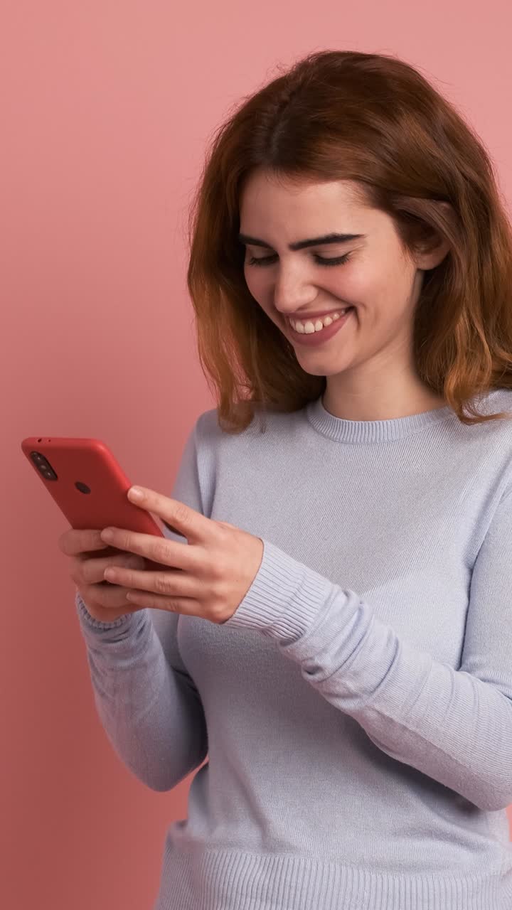 Smiling woman using mobile phone in pink studio. Vertical Footage