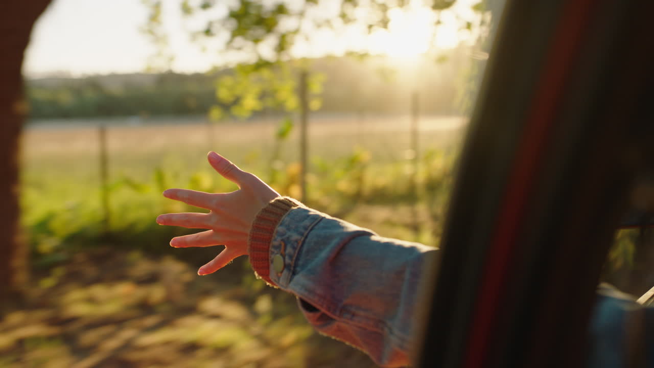 차 안에서 손을 밖으로 내밀고 창문을 들고 손가락을 통해 바람이 불고 시골에서 여행하는 여름 휴가 도로 여행 해가 지는 도로에서 자유를 즐기는