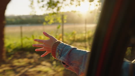 mujer en el coche con la mano afuera de la ventana sintiendo el viento soplando a través de los dedos conduciendo en el campo viajando en vacaciones de verano viaje por carretera disfrutando de la libertad en la carretera al atardecer