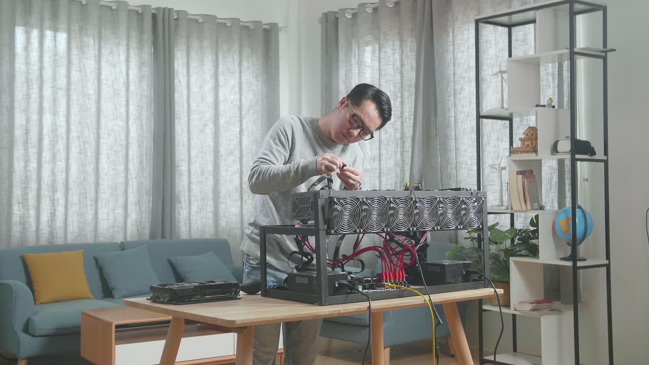 안경을 쓴 아시아 남자가 암호화폐를 채굴하기 위해 광산 기지의 전원 케이블을 연결합니다.