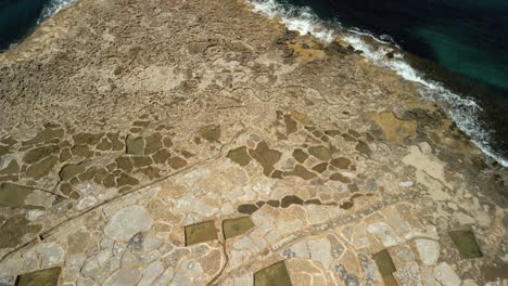 upwards aerial views of the salt pans of xwejni on gozo island in malta showing the salt flats and sea waves crashing against the coast