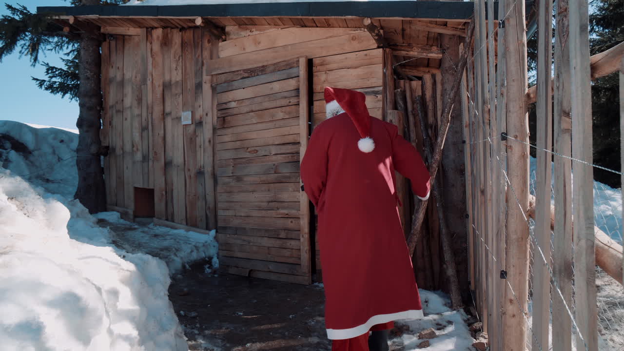santa camina hacia una pequeña cabaña de madera y hay una gran cantidad de nieve a un lado