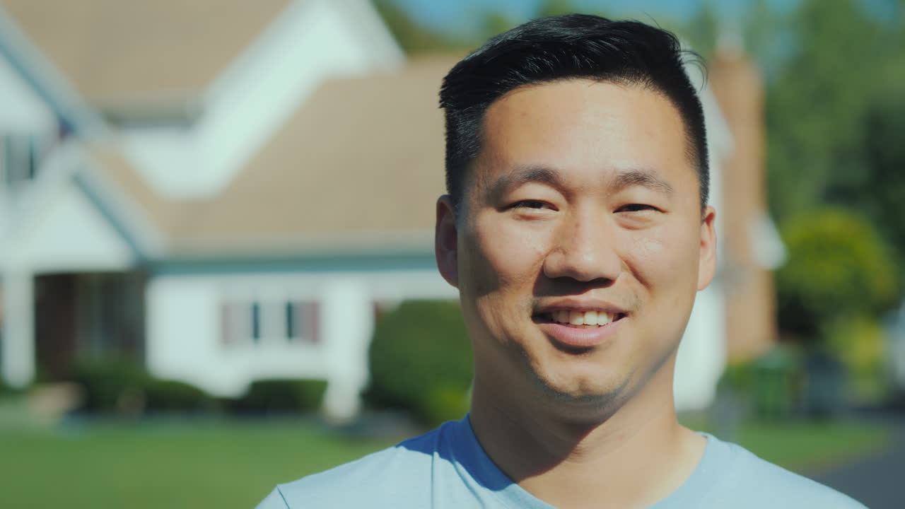 집에서 흐릿한 배경을 배경으로 카메라를 바라보며 웃고 있는 젊은 아시아 남자의 초상화