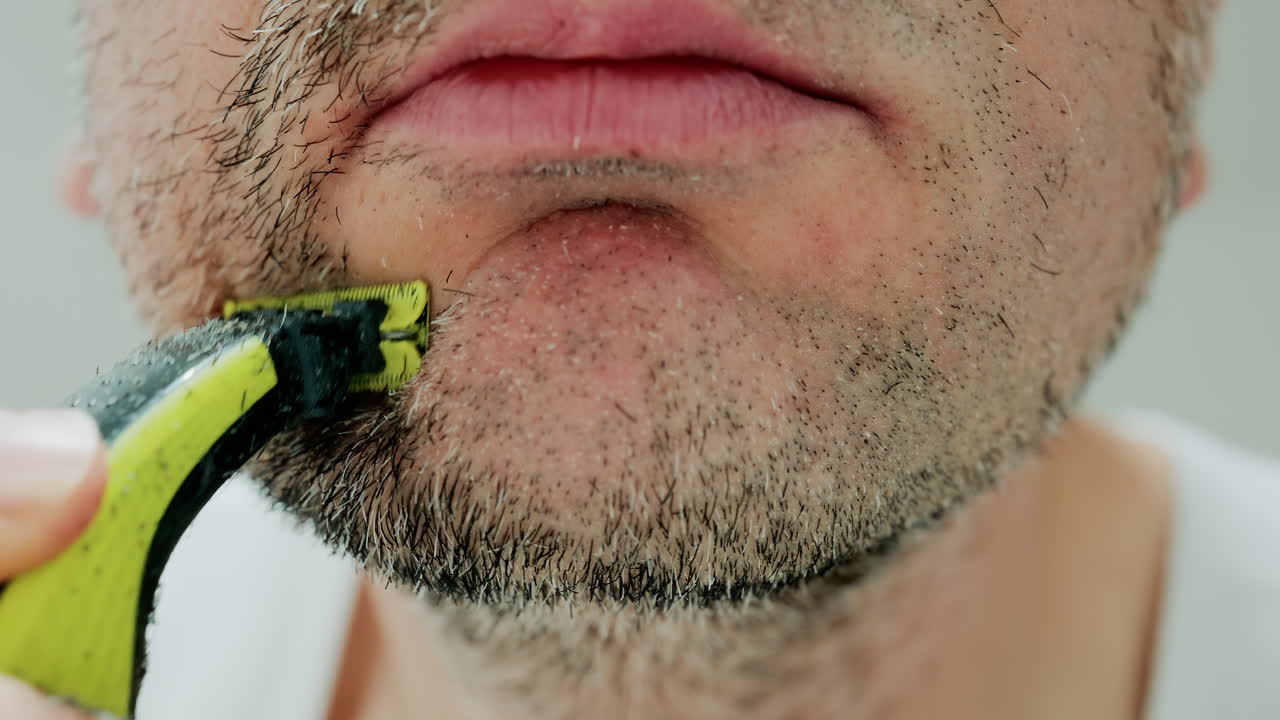 Close up of a man using an electric razor to trim facial hair in the bathroom